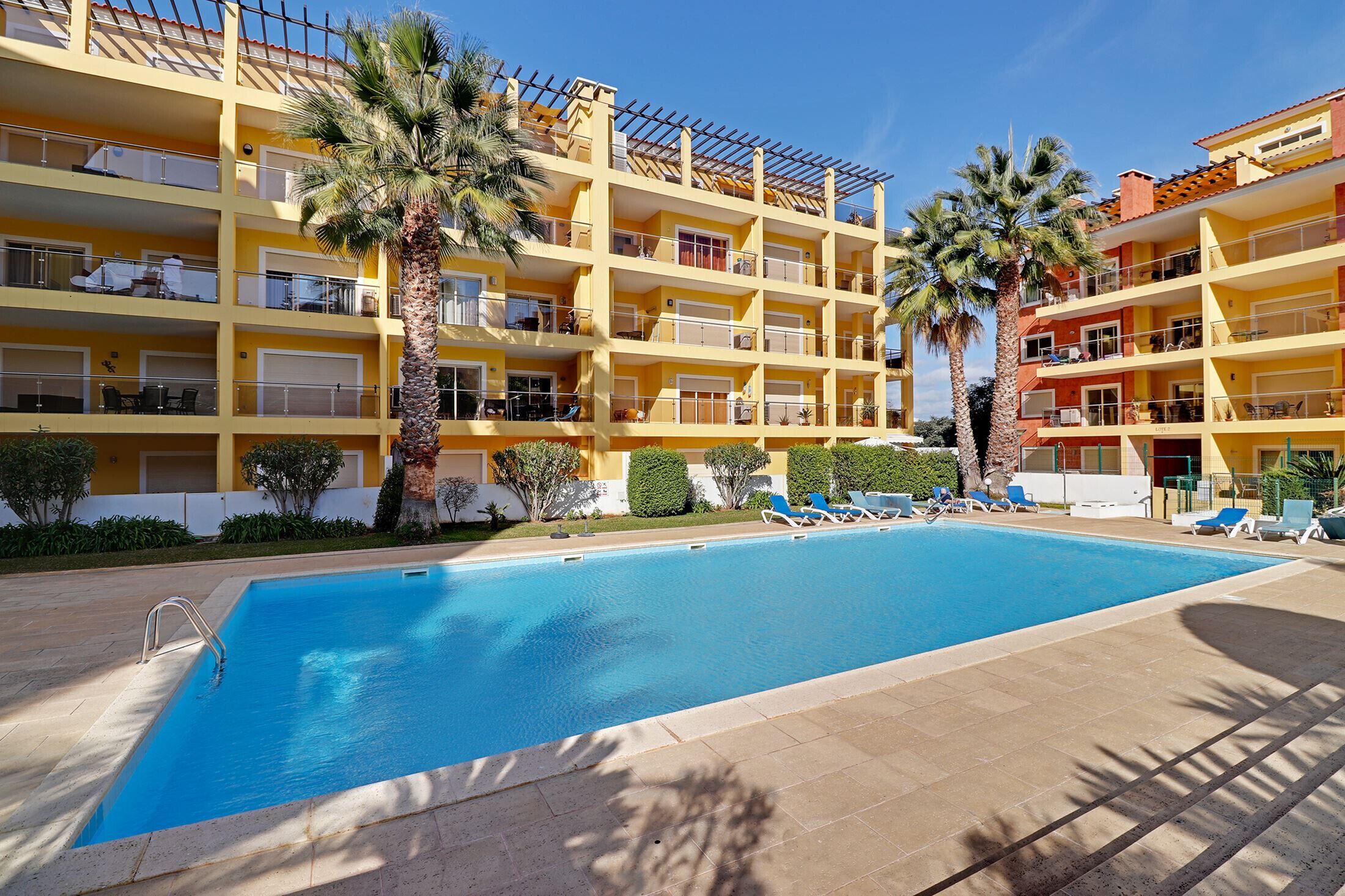 Un hotel con piscina, varios balcones y palmeras.