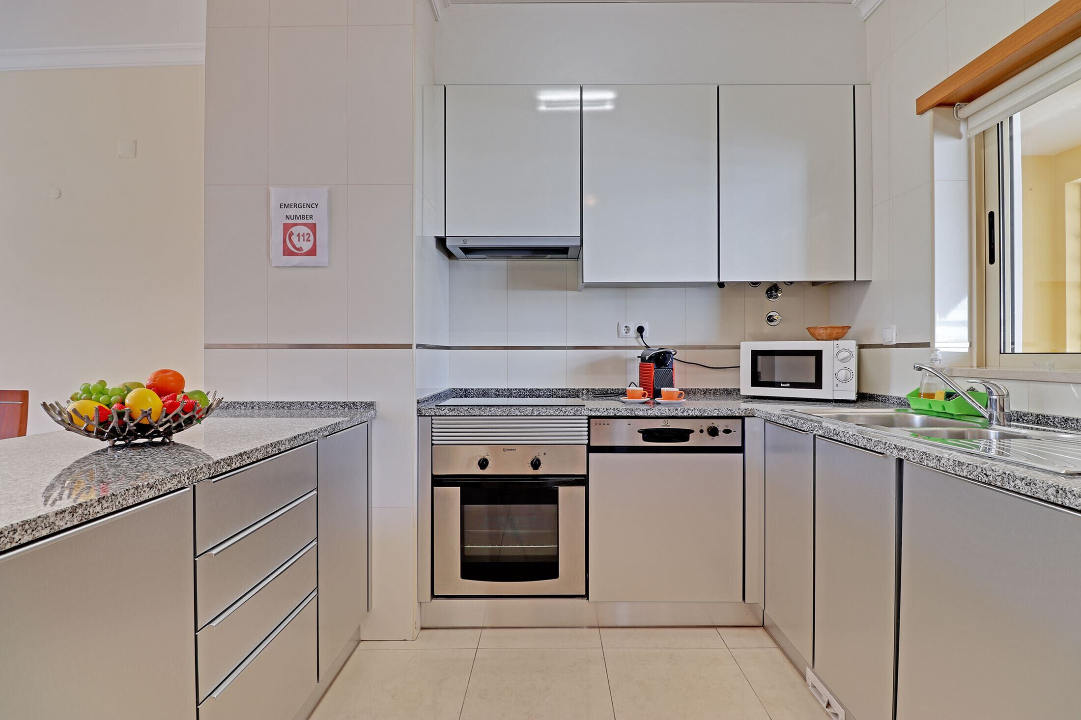 Cocina compacta con horno empotrado, microondas y frutero en la encimera.