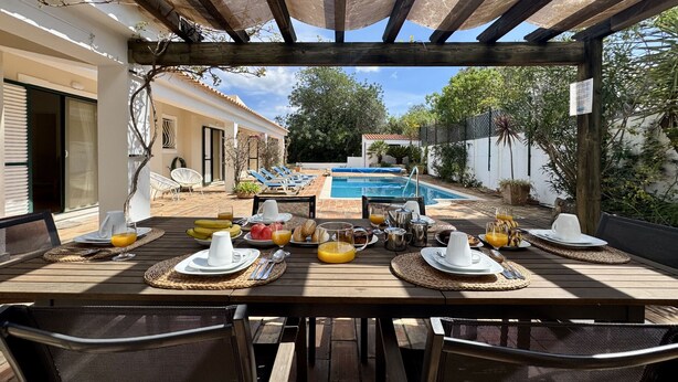 A wooden table set for breakfast with a pool in the background. - Algarve Country Villa With Pool (Sao Bras de Alportel)