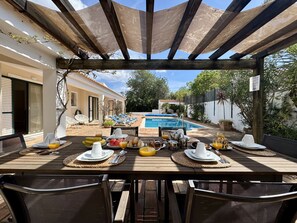 Une table en bois, dressée pour le petit-déjeuner, avec une piscine en arrière-plan.