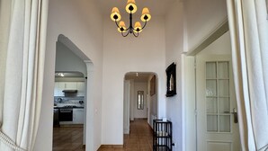 A hallway with a chandelier, a door with glass panels, and a kitchen visible through an archway. - Algarve Country Villa With Pool (Sao Bras de Alportel)