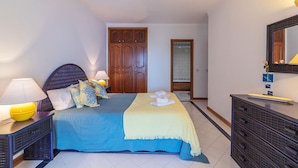 Um quarto com uma cama, mesas de cabeceira, cômoda, espelho e guarda-roupa.