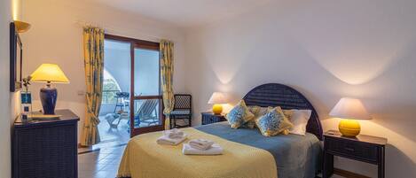 A bedroom with a bed, two bedside tables with lamps, a chair, a window with curtains, and a balcony.