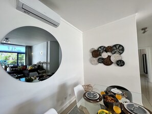 A modern living room with a circular mirror, a dining area with a glass table, and a wall-mounted decorative piece.