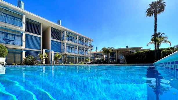 Ein Schwimmbad mit klarem, blauem Wasser, umgeben von einem modernen Gebäude mit mehreren Balkonen und einer Palme.