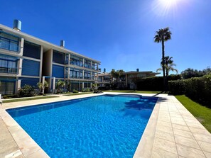 A modern hotel with a swimming pool, multiple balconies, and a clear blue sky.