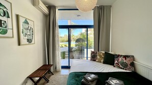 Ein Schlafzimmer mit Bett, Kissen, einer Bank und Blick auf ein Schwimmbecken und Grünfläche.