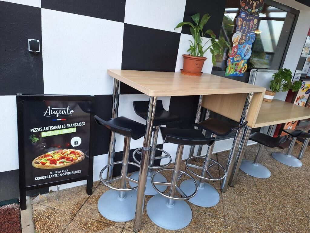 Interior de un restaurante con pared de baldosas blancas y negras en damero, una mesa de madera y taburetes de metal.