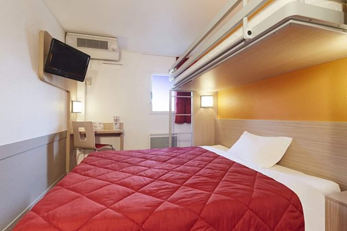 A hotel room with a bed, a television mounted on the wall, a desk with a chair, and a window.