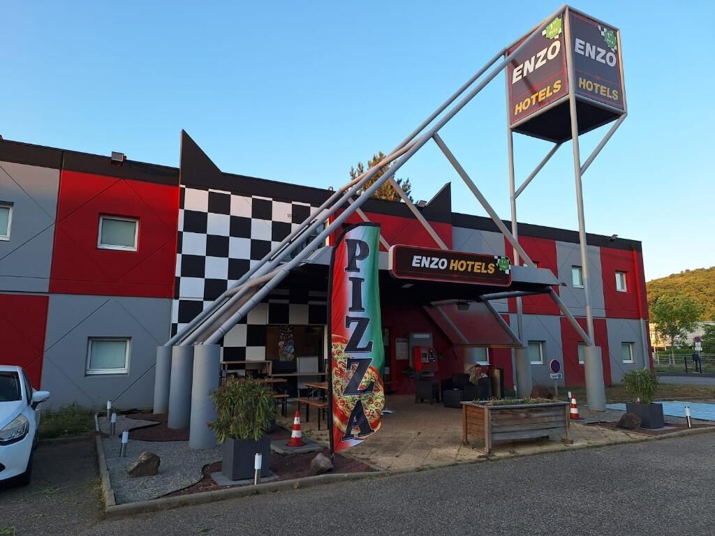 Een gebouw met een geruit gevel, een groot bord met pizza erop en een bord voor Enzo Hotels.