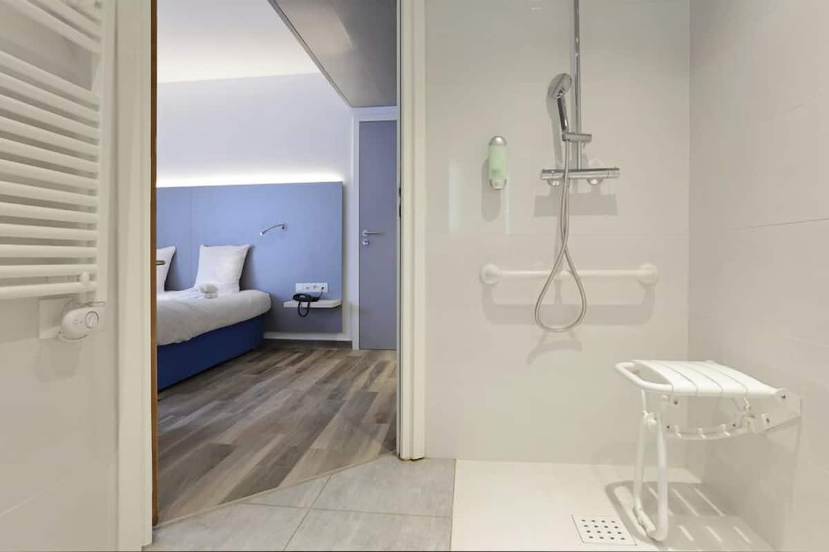 A modern bathroom with a shower, a toilet, and a small bedside table with a lamp.