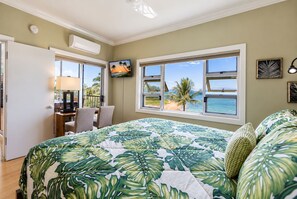 A bedroom with a large bed, a desk, and a chair, with a view of the ocean through the windows. - Pure Luxury Kihei Rare 3BR Oceanfront Condo Freshly Redesigned Ocean Views (Kihei)