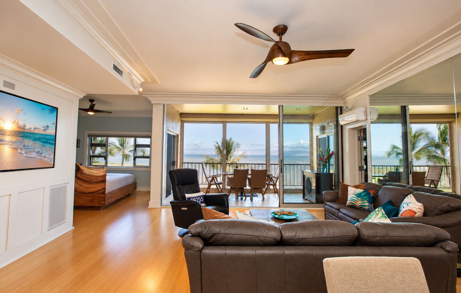 A spacious living area with a large sofa, a dining table, and a balcony with a view of the ocean.
