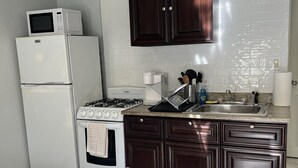 Une cuisine compacte équipée d’une cuisinière, d’un four à micro-ondes et d’un réfrigérateur. Le sol est recouvert d’un tapis à motifs et les meubles sont en bois foncé.