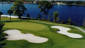 Ein Golfplatz mit Sandbunkern, einem Wasserhindernis und einer entfernten Küstenlinie mit Gebäuden.