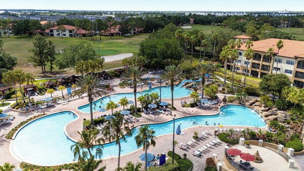 A resort with a large pool, palm trees, and a golf course in the background.