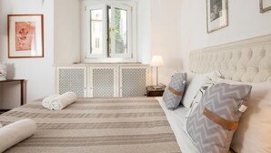 A bedroom with a large bed, a window with a view, a bedside table with a lamp, and a decorative headboard. - Aurora in Pantheon Apartment (Rome)