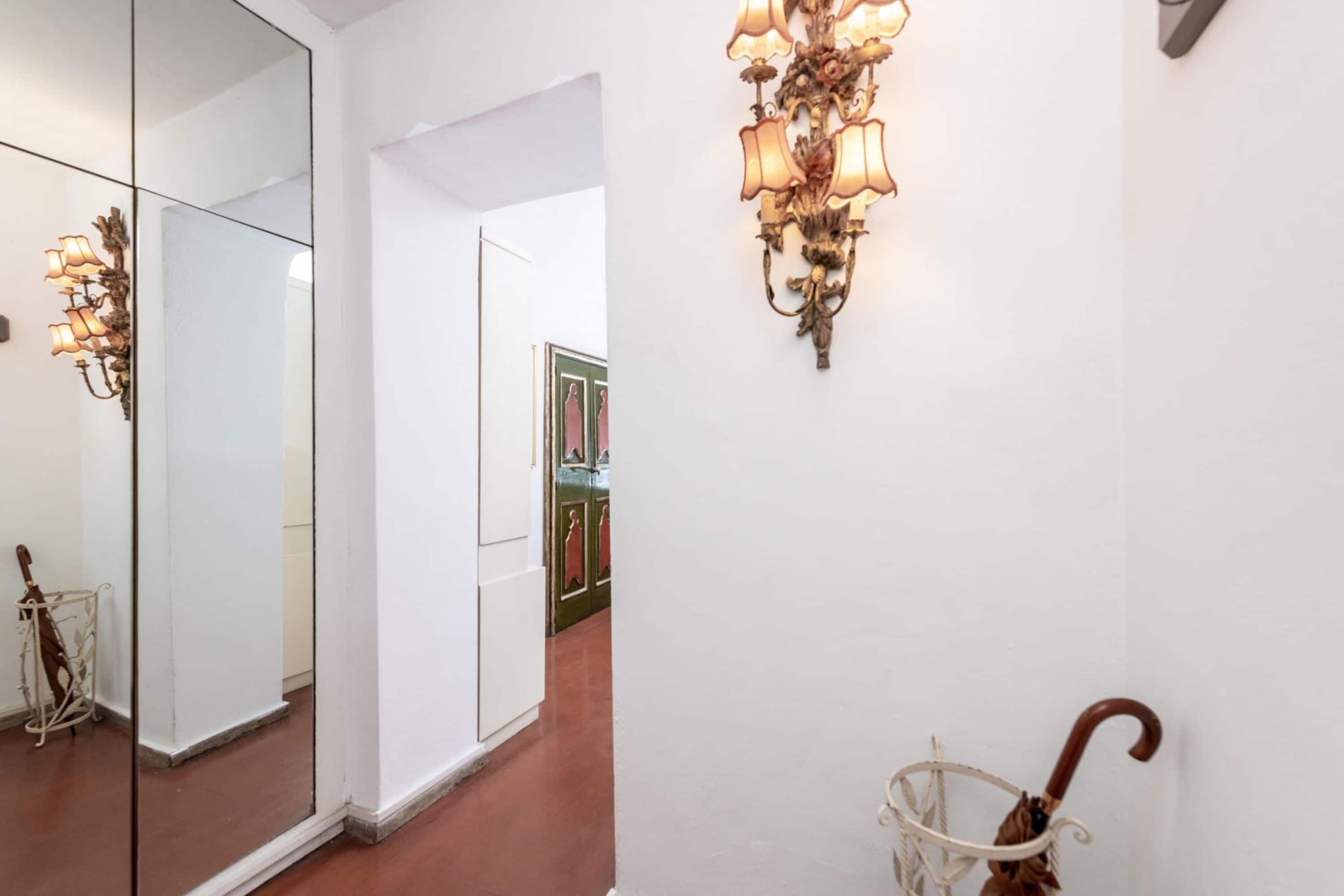 A hallway with a mirror, a wall-mounted light fixture, and a wicker basket with an umbrella.