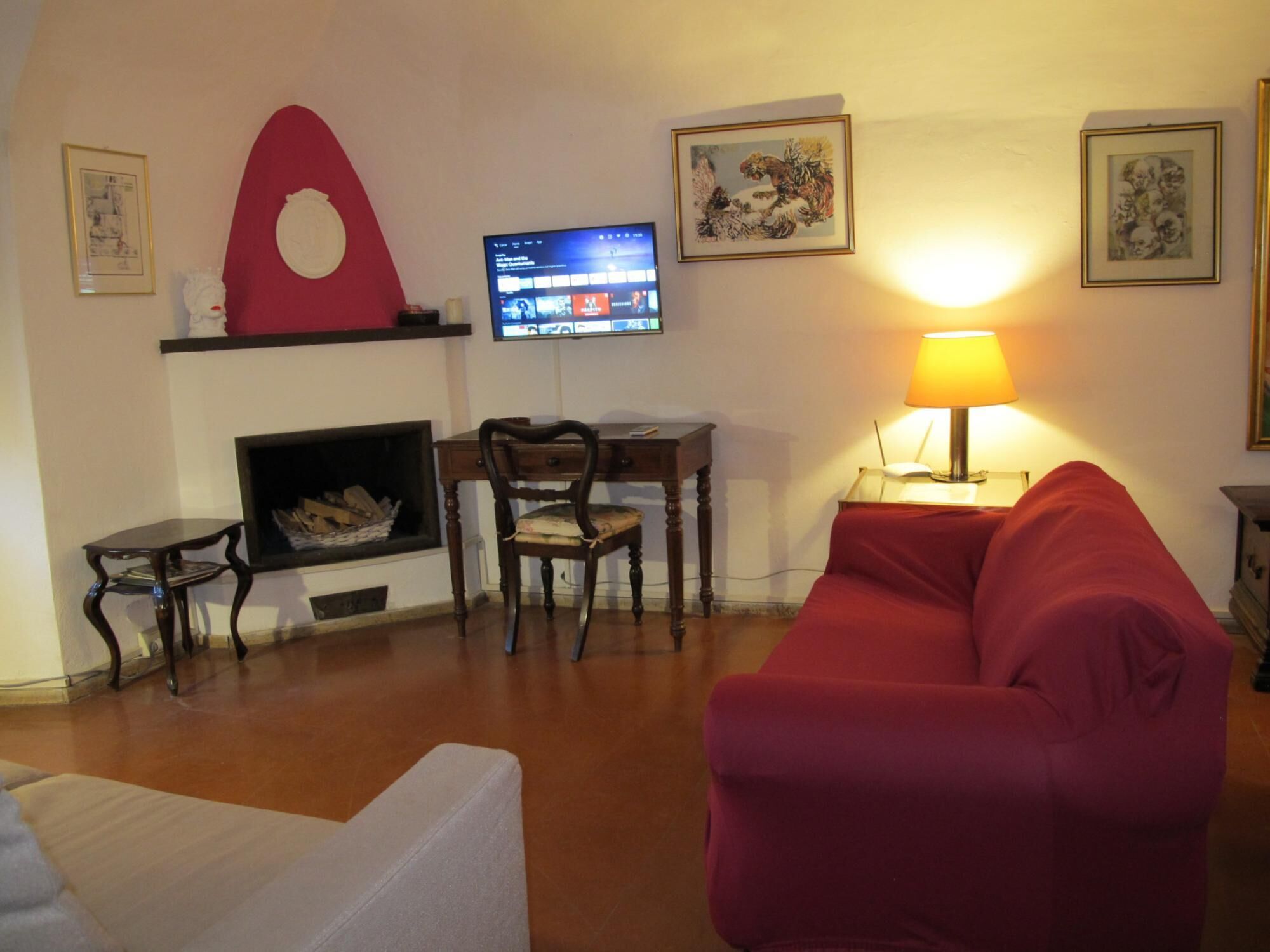 Ein Wohnzimmer mit Kamin, Fernseher, einem roten Sofa und einer Lampe.