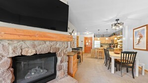 Una sala de estar moderna con chimenea de piedra, un televisor de pantalla plana montado encima y un comedor con muebles de madera.