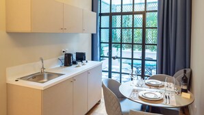 A compact kitchen with a sink, cabinets, and a dining area with a table set for two. - Queen Suite By 33Solonos Suites (Athina)