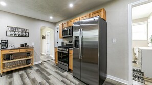 A modern kitchen with a stainless steel refrigerator, wooden cabinets, a coffee bar, and a microwave. - Boho Inspired 3 bed/2 bath (Lansing)