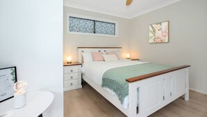 Un dormitorio con cama, mesitas de noche, ventilador de techo y obras de arte en las paredes.
