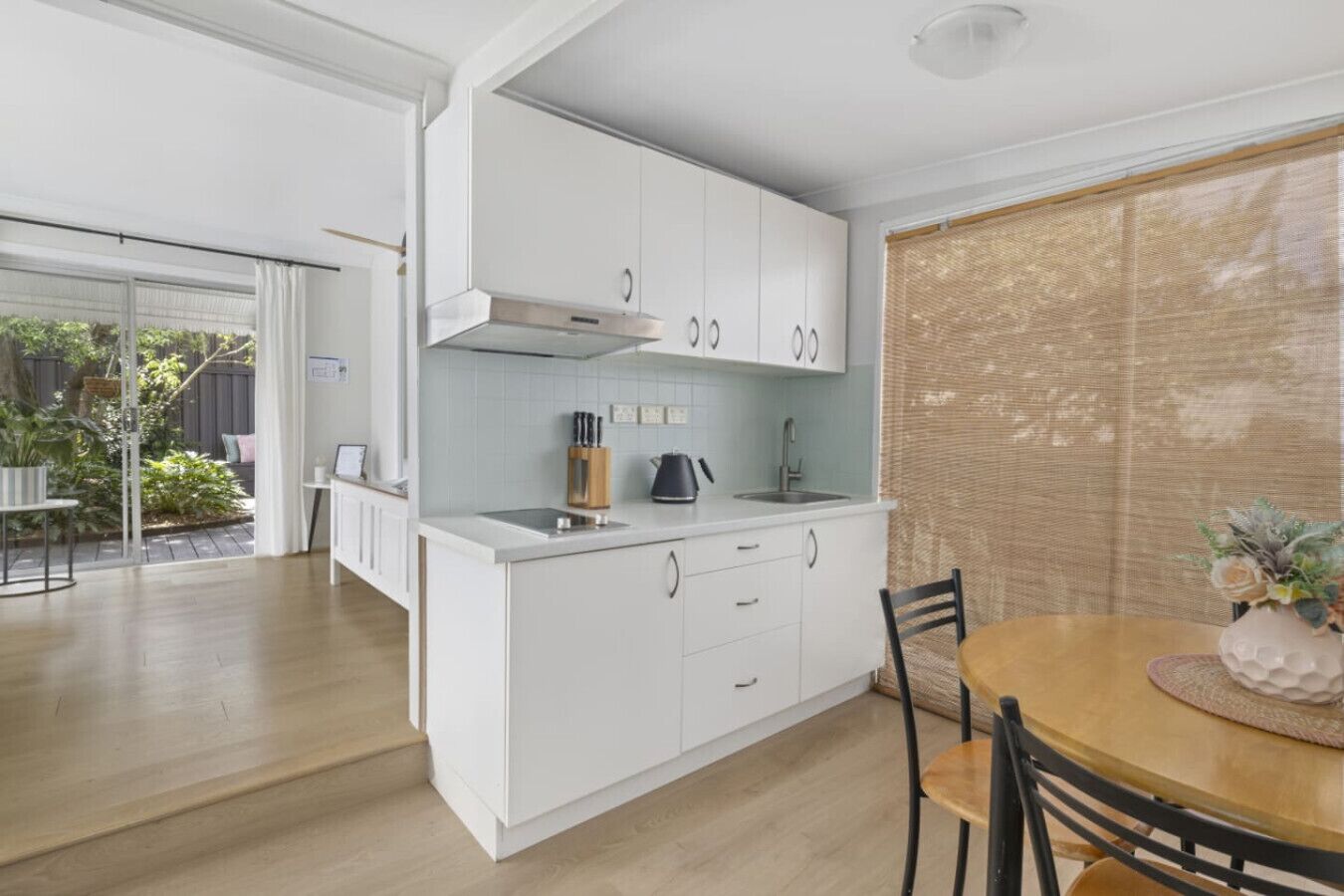 A modern kitchen with white cabinets, a central island, and a dining area with a wooden table and chairs.