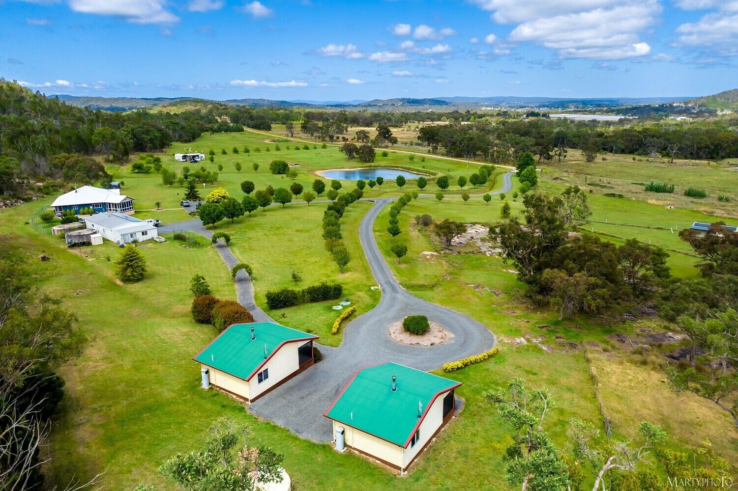 A large, open property with multiple buildings, a winding driveway, and a pond.