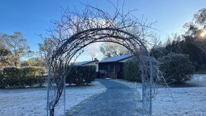 A gravel pathway leading to a wooden house with a metal archway, surrounded by snow-covered ground and sparse trees. - Stargazers Escape Stanthorpe (Diamondvale)