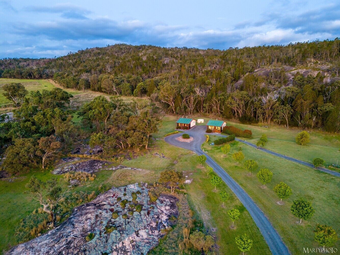 A rural landscape with a winding road leading to a cluster of buildings with green roofs.