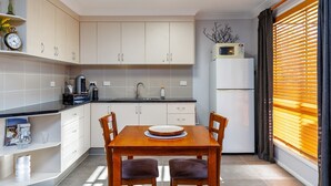 A compact kitchen with white cabinets, a dining table with chairs, a microwave, and a refrigerator. - Stargazers Escape Stanthorpe (Diamondvale)