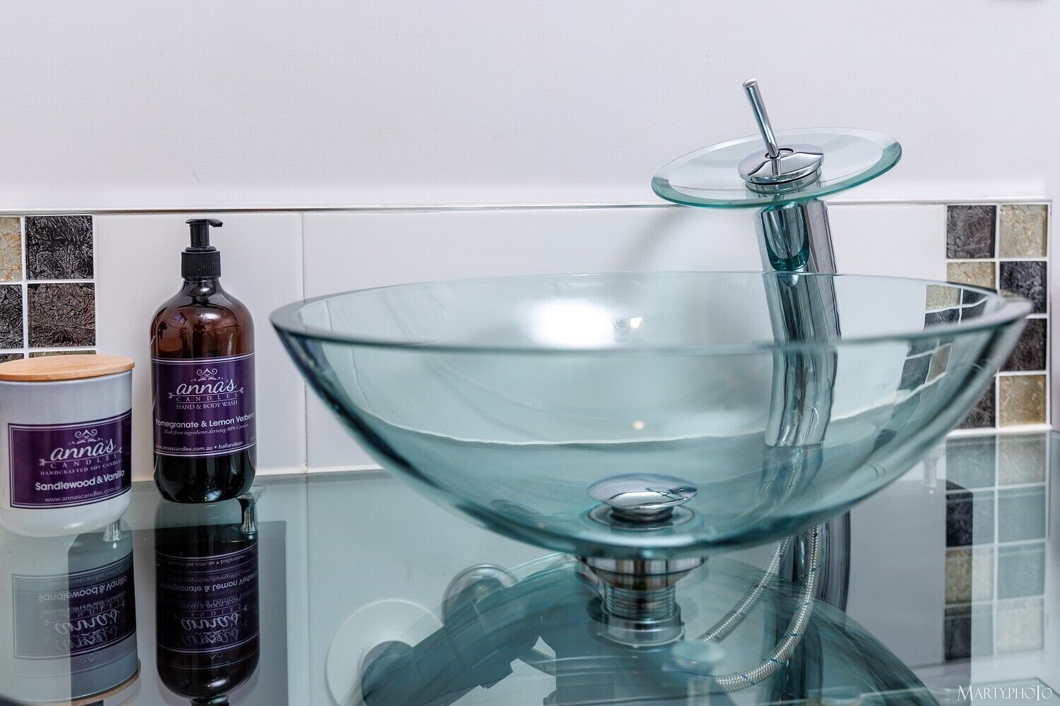 Une salle de bain avec un lavabo en forme de bol en verre, un distributeur de savon et une bougie.