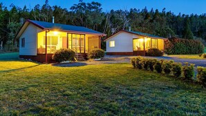 Two single-story houses with large windows and a covered porch, surrounded by a well-maintained lawn and dense trees. - Stargazers Escape Stanthorpe (Diamondvale)