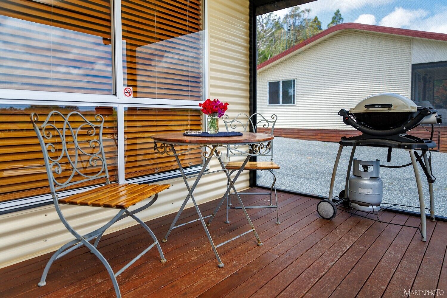 Un patio techado con una mesa y sillas de metal, una parrilla y un tanque de gas.