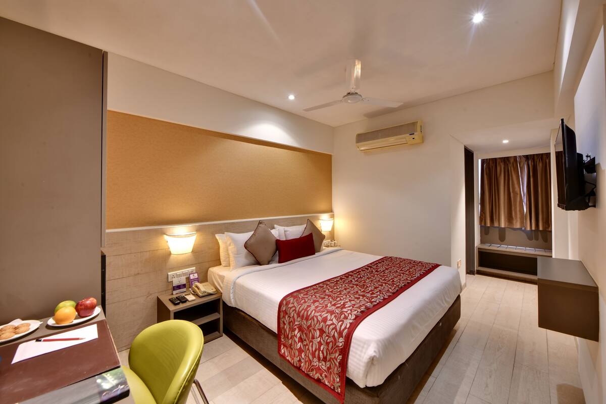 A hotel room with a bed, bedside table, chair, desk, and a TV mounted on the wall.