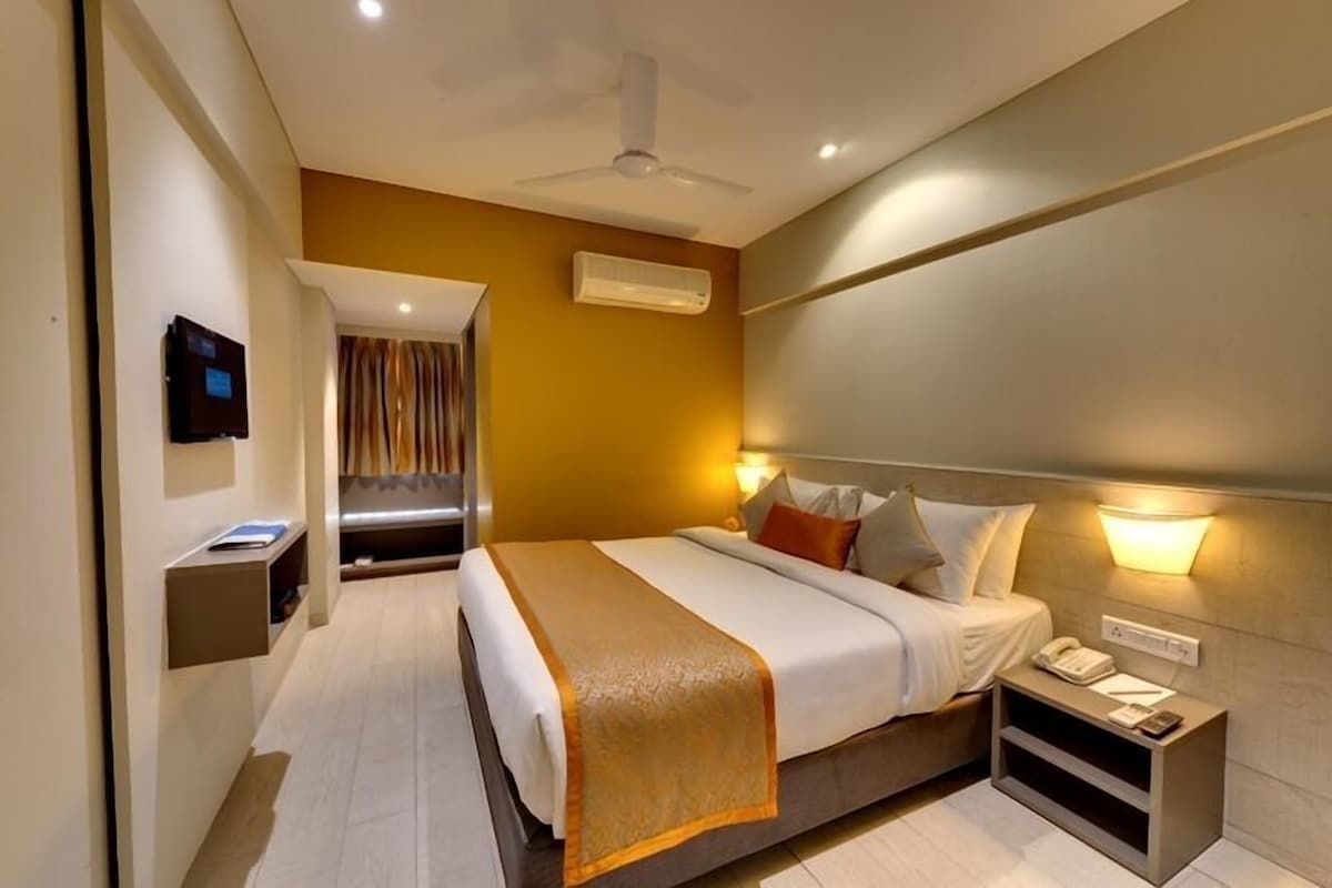 Una habitación de hotel con cama, mesita de noche, televisor montado en la pared y aire acondicionado.