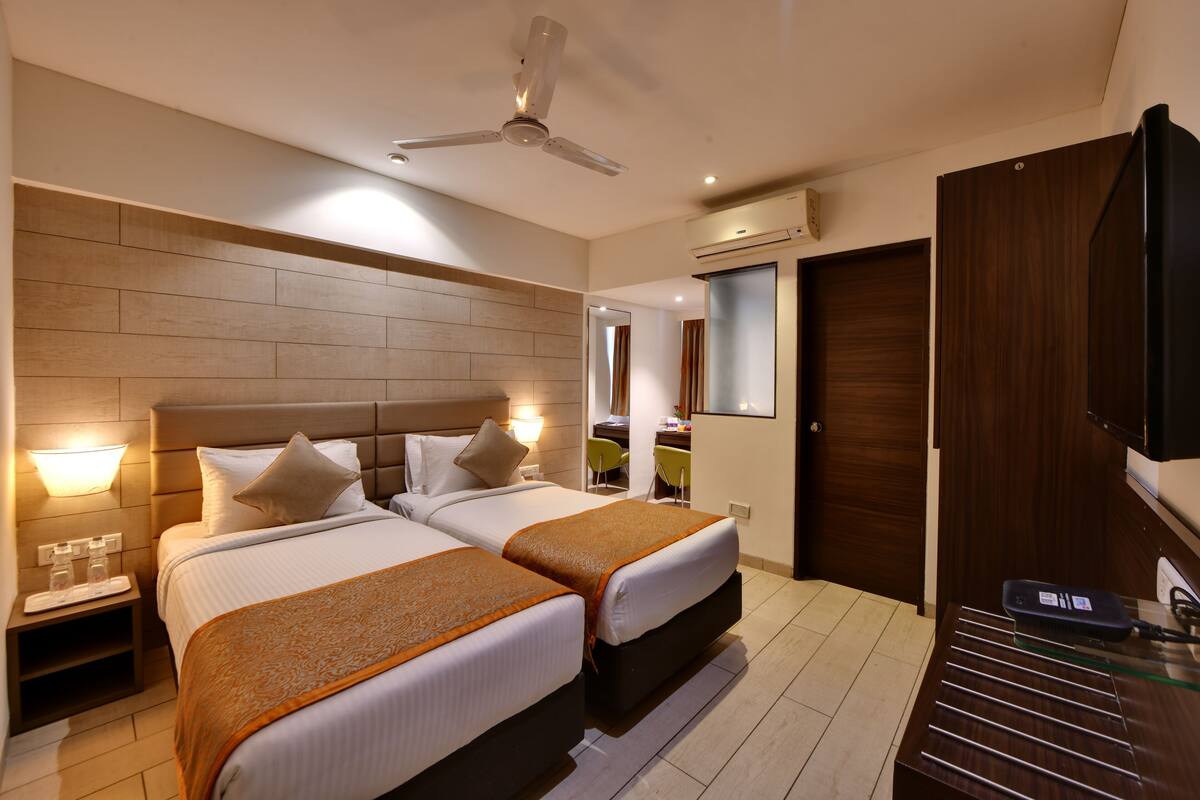 A hotel room with two beds, a ceiling fan, a desk, a chair, and a TV.