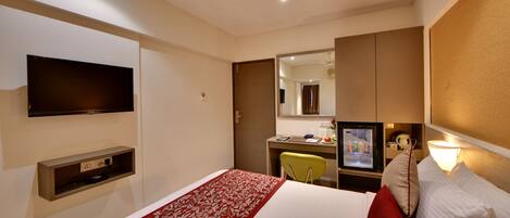 Habitación de hotel con una cama, un escritorio con computadora, un televisor en la pared y un espejo sobre el escritorio.