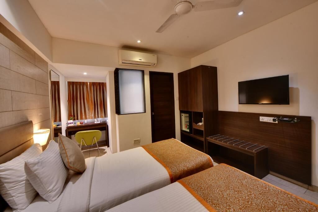 Habitación de hotel con dos camas, un escritorio, una silla, un televisor y un armario.