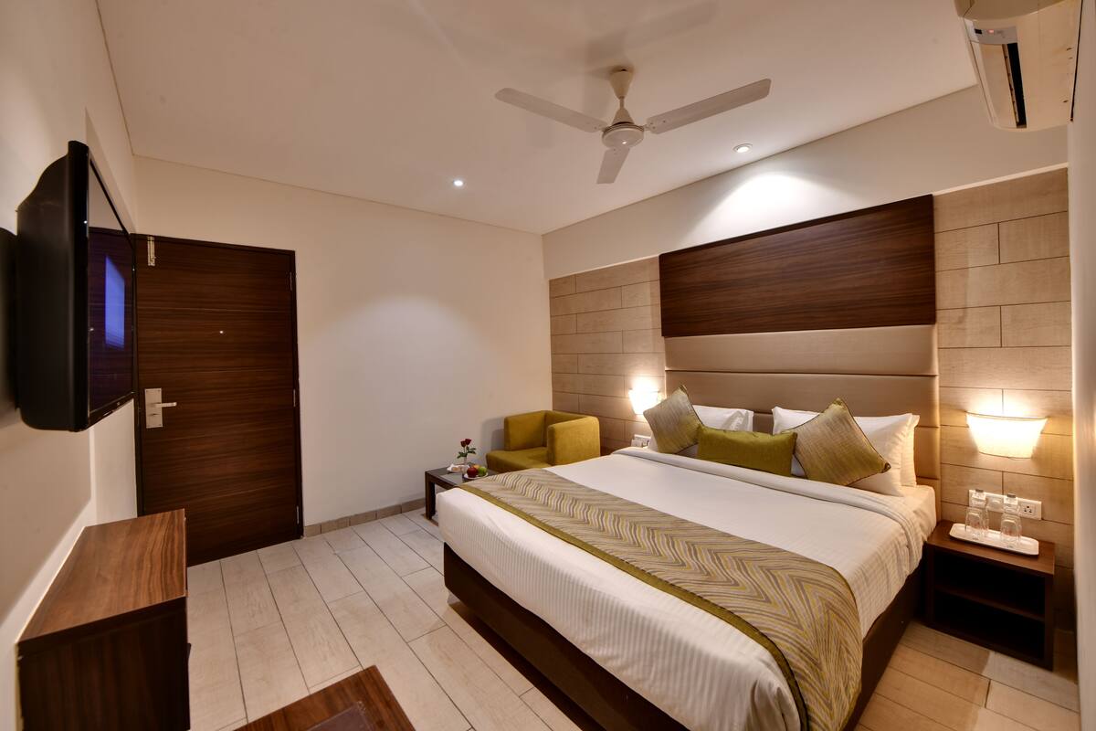 A modern hotel room with a large bed, a ceiling fan, a flat-screen TV, and a bedside table with a lamp.