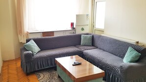 Un salon avec un canapé d’angle, une table basse en bois et une fenêtre avec des rideaux.