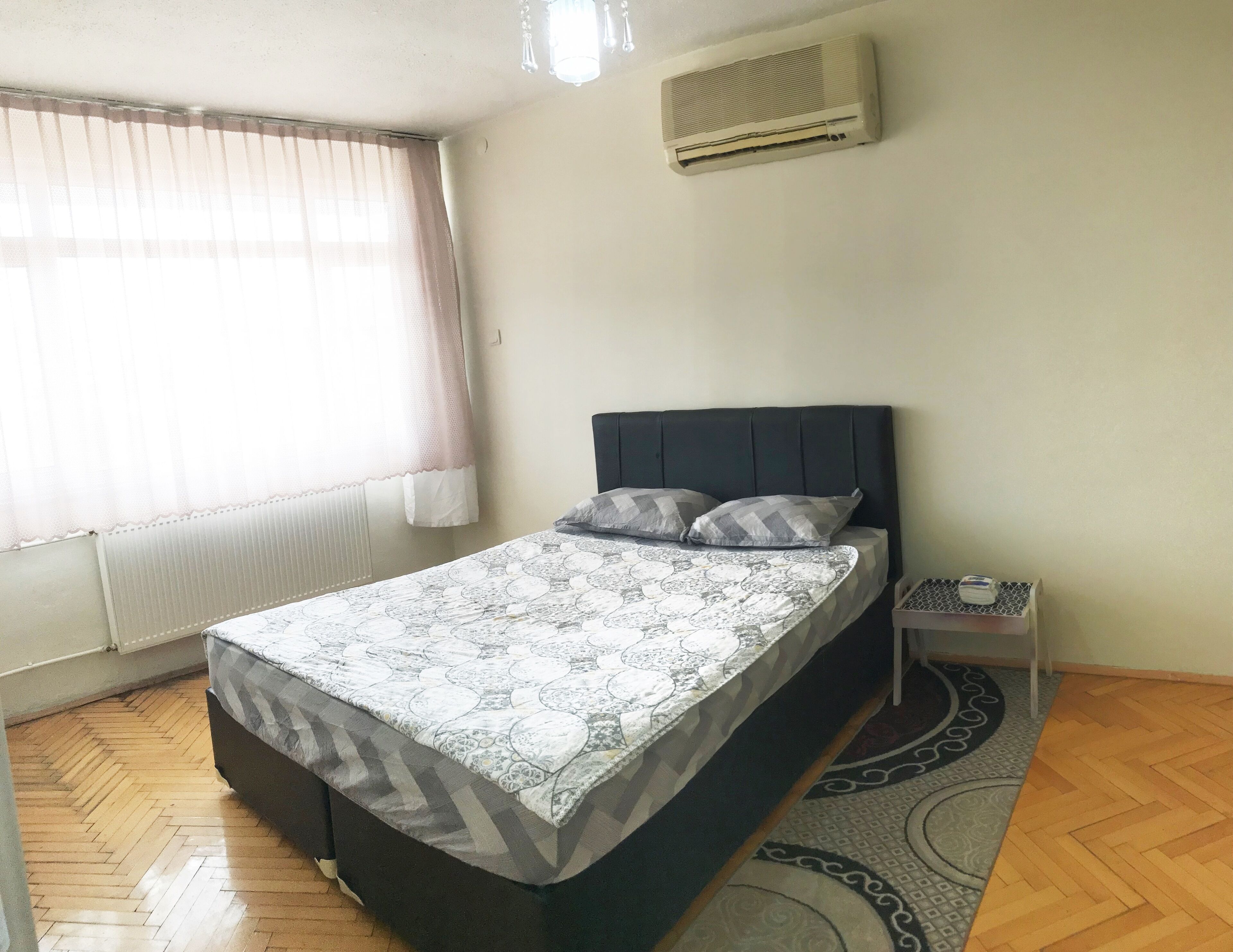 Quarto com cama, mesa de cabeceira, aquecedor e janela com cortinas.
