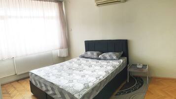 Quarto com cama, mesa de cabeceira, aquecedor e janela com cortinas.