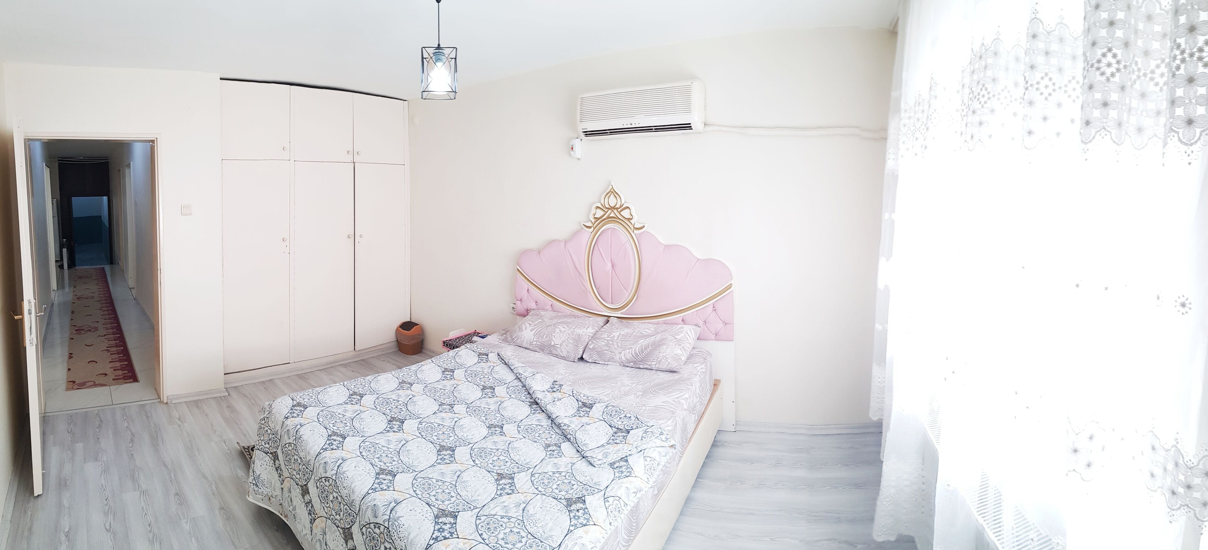 A bedroom with a bed, a wardrobe, a hanging light, and an air conditioning unit.