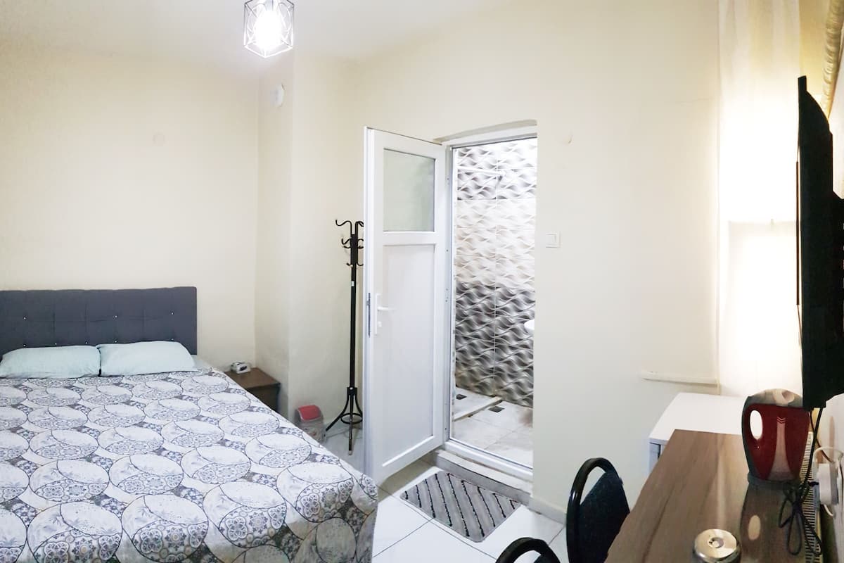Une chambre à coucher comprenant un lit, un bureau, une chaise, un téléviseur et une porte donnant sur un balcon.