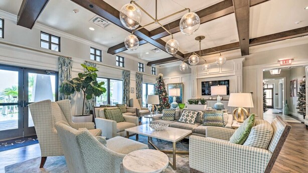 A spacious lobby with a high ceiling, large windows, and a Christmas tree. There are multiple seating areas with patterned furniture and a central coffee table.
