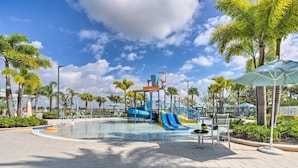 A pool area with a water slide, lounge chairs, and palm trees.