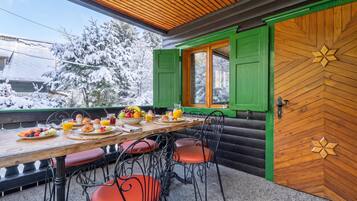 A breakfast table set with fruits, eggs, and juice, with a view of snow-covered trees outside.