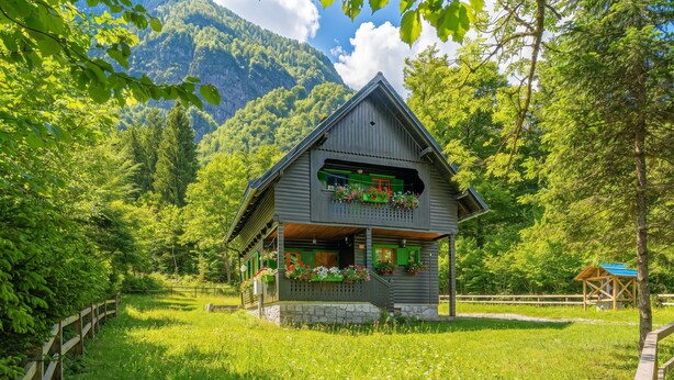 A wooden chalet with a balcony, surrounded by lush greenery and mountains. - Alpine Chalet Metka at Lake Bohinj (Bohinj)
